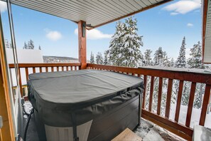 Un bain à remous sur une terrasse en bois, avec vue sur un paysage enneigé.