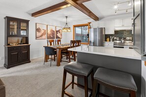 A modern kitchen with a central island, wooden chairs, and a dining table. - Big White Ski-In/Ski-Out Townhome | Private Hot Tub + Mountain Views (Kootenay Boundary E / West Bo*)