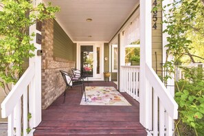 Eine überdachte Veranda mit Holzboden, zwei Stühlen, einem Blumentopf und einem weißen Geländer.