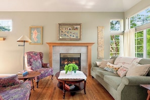 A living room with a fireplace, a green sofa, a floral armchair, a small round table with a vase, and a lamp. - Spacious 2400 sq ft NoBo Home: Restaurants - Hiking - Trails - Quiet (Boulder)