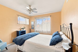 A bedroom with a bed, a ceiling fan, two windows with curtains, a bedside table with a plant, and a wall-mounted lamp. - Spacious 2400 sq ft NoBo Home: Restaurants - Hiking - Trails - Quiet (Boulder)
