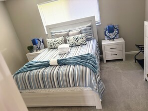 A neatly made bed with striped bedding, a bedside lamp, and a nightstand with a lamp and a decorative item. -  Welcome to The Tropics (Cape Coral)