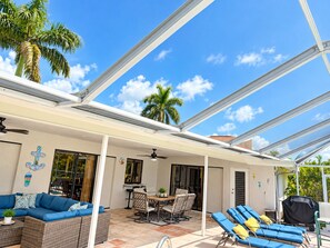 A covered outdoor patio with a dining area, lounge chairs, and a ceiling fan. -  Welcome to The Tropics (Cape Coral)