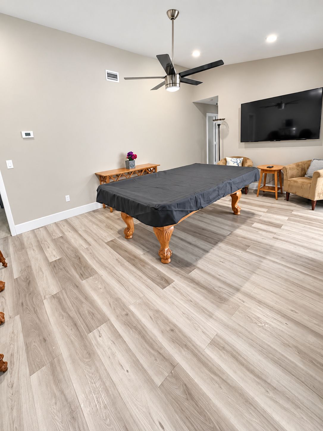 A room with a pool table, a ceiling fan, a flat-screen TV, and a wooden floor.