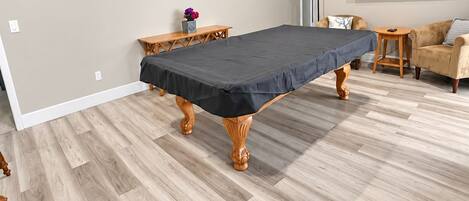 A room with a pool table, a ceiling fan, a flat-screen TV, and a wooden floor.