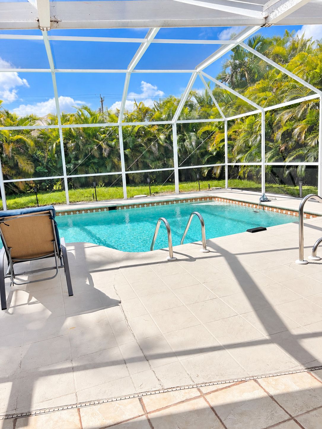 A covered swimming pool with clear blue water, surrounded by lush greenery and a white roof structure.