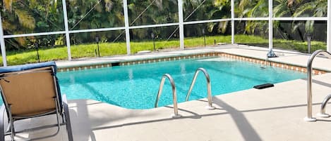 A covered swimming pool with clear blue water, surrounded by lush greenery and a white roof structure.