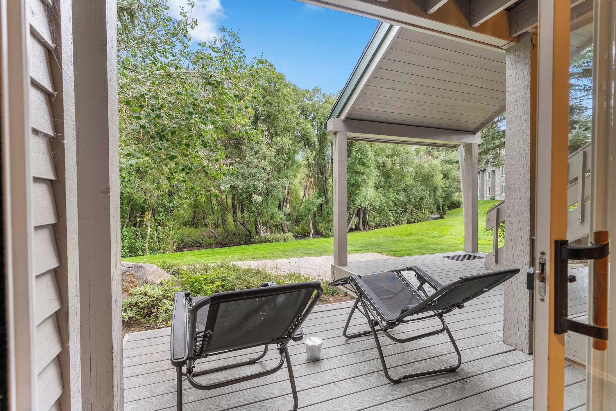 An open covered patio with two lounge chairs and a view of a green landscape.