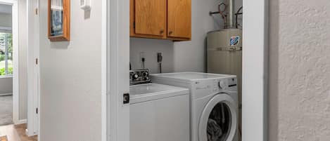 A laundry room with a front-loading washer and dryer, wooden cabinets above, and a water heater to the right.