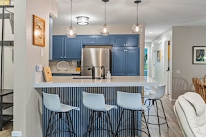 A modern kitchen with blue cabinets, a stainless steel refrigerator, and a bar area with stools. - 2BR Condo for 6 w Shared Hot Tub, Near Mtn & Lakes (Mammoth Lakes)