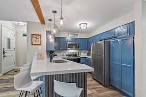 A modern kitchen with blue cabinets, stainless steel appliances, a white island with bar stools, and pendant lighting. - 2BR Condo for 6 w Shared Hot Tub, Near Mtn & Lakes (Mammoth Lakes)