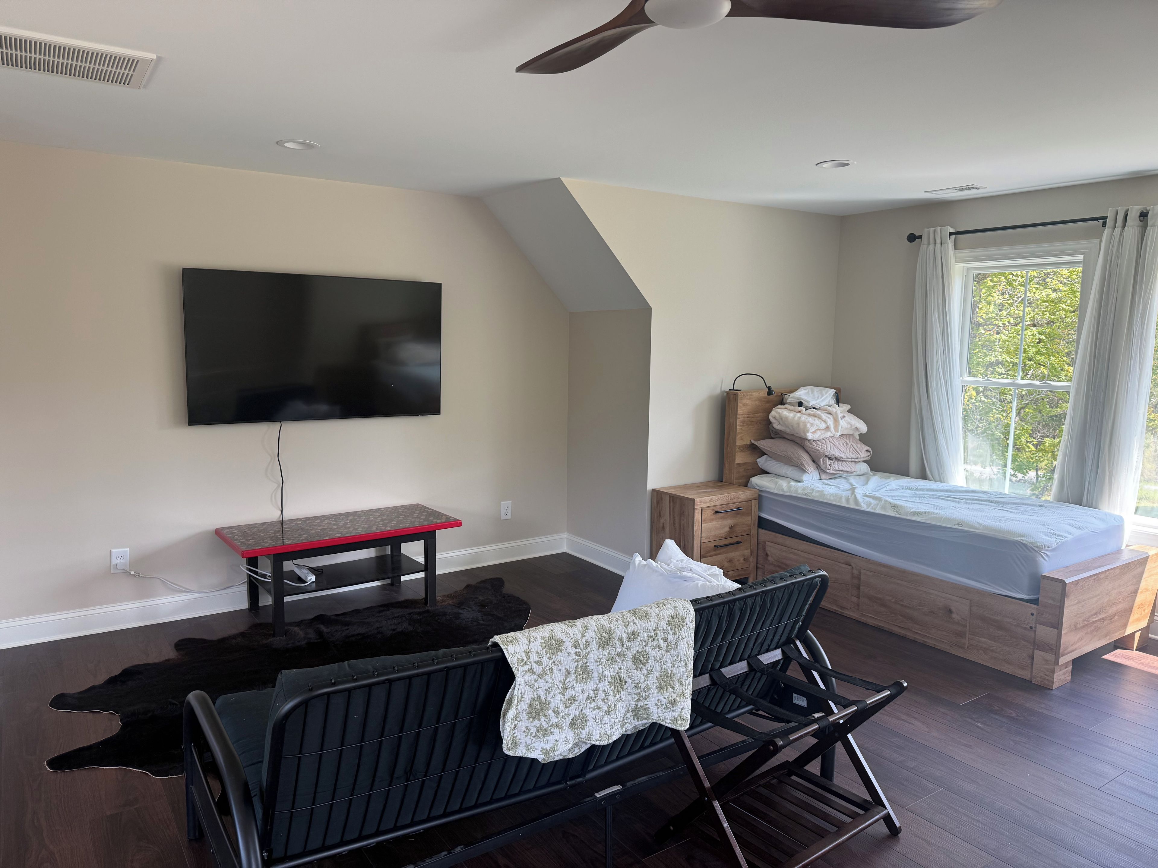 A bedroom with a bed, a TV, a desk, and a window.