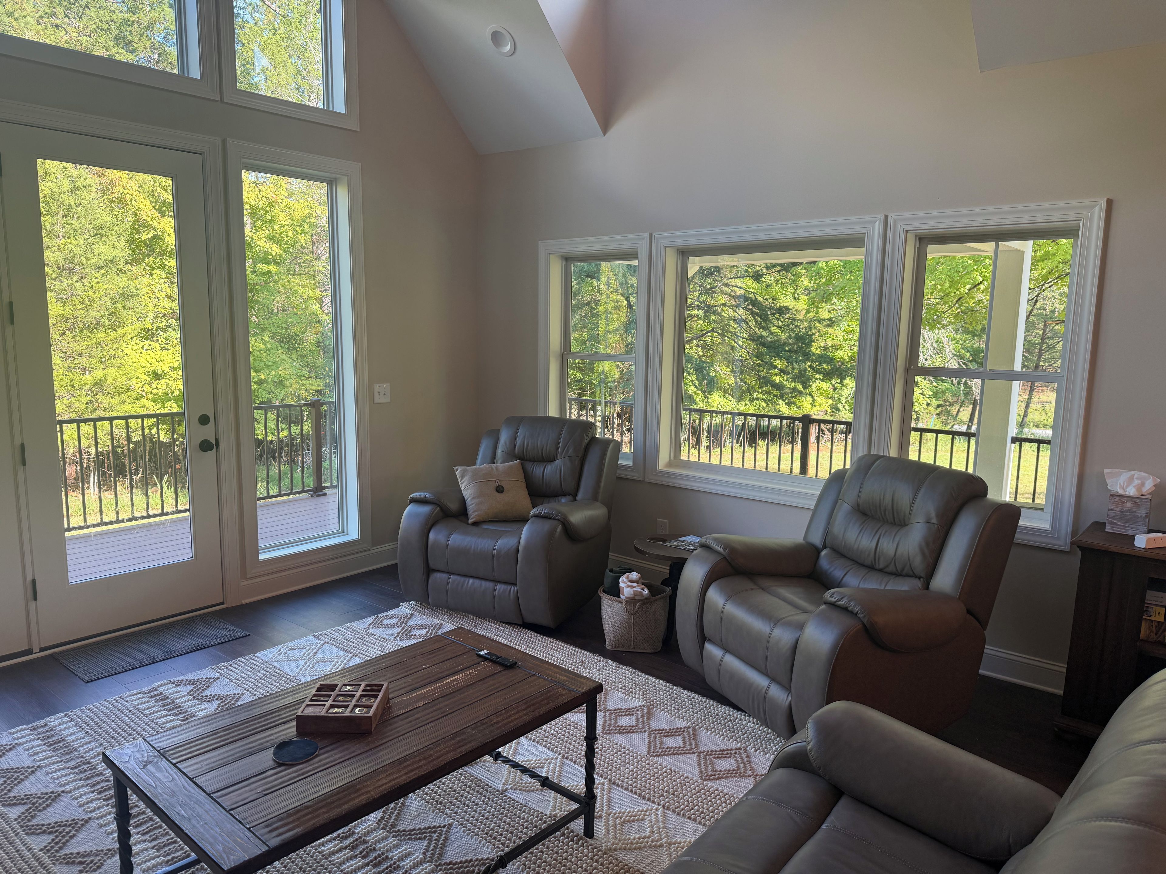 A spacious living room with a high ceiling, large windows, and a view of the outdoors.