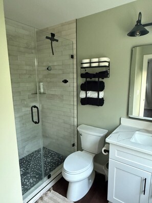 A bathroom with a glass-enclosed shower, a white toilet, a sink with a marble countertop, and a towel rack with towels. - Attn Race Teams: Brand New 3-Bedroom 3.5 Bathroom House - 10 minutes to VIR Gate (Semora)