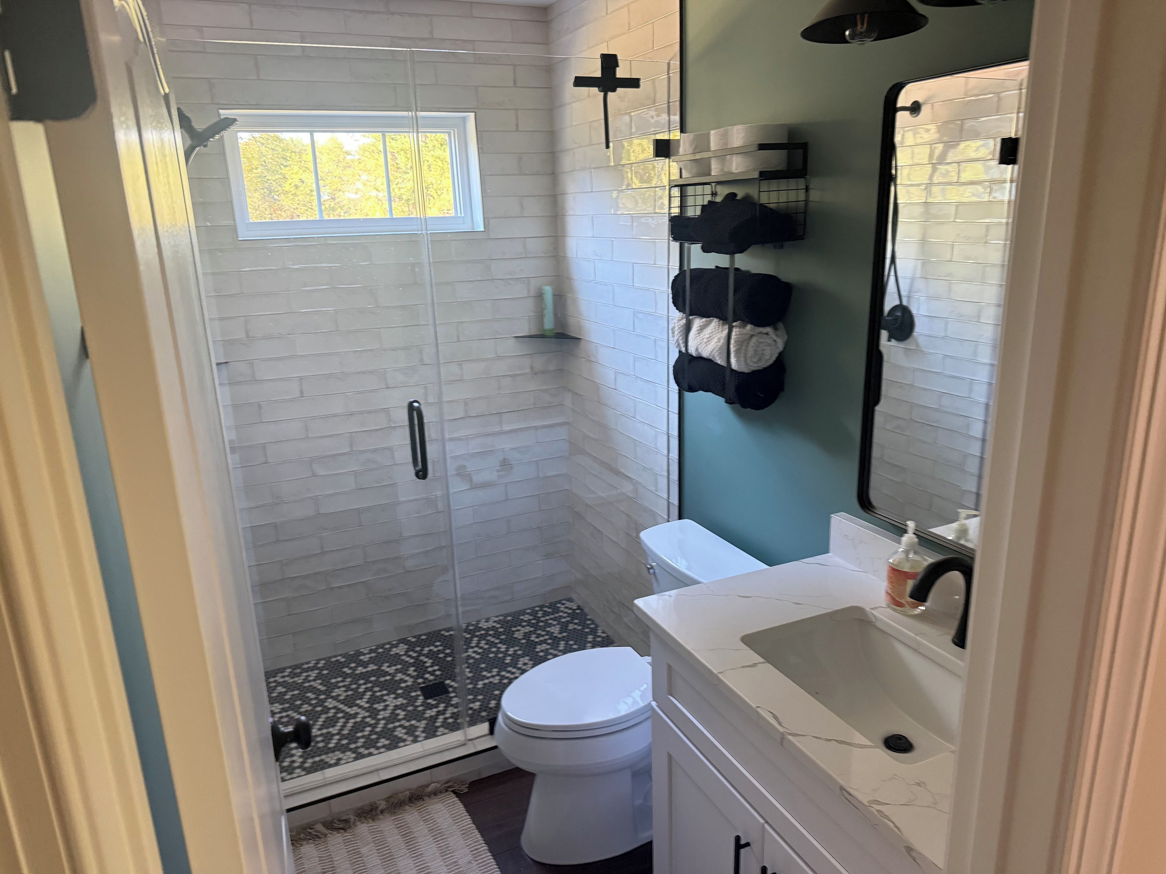 A bathroom with a glass-enclosed shower, a toilet, a sink, and a towel rack.