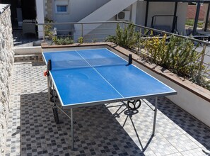 Ein tragbarer Tischtennis-Tisch auf einer gefliesten Terrasse mit Geländer und Blumentöpfen.