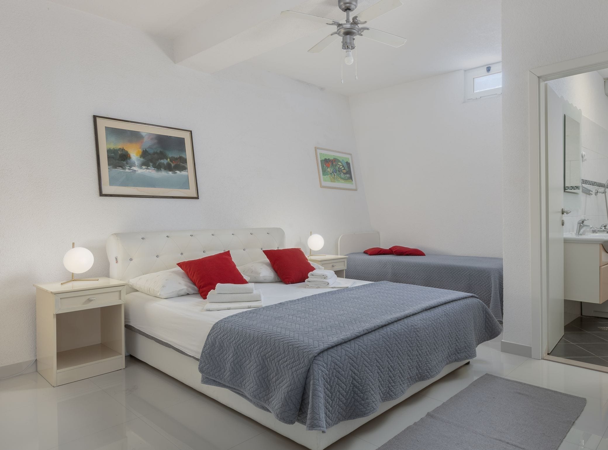 A hotel room with a bed, bedside tables, a ceiling fan, and artwork on the walls.
