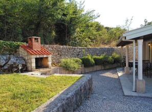 A stone-built outdoor kitchen with a chimney, surrounded by a stone wall and greenery. - One Bedroom Holiday Home with Terrace (Gruda)