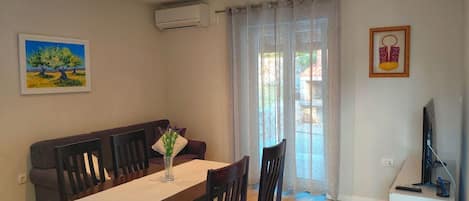 A dining area with a table, chairs, a sofa, and a TV on a stand.