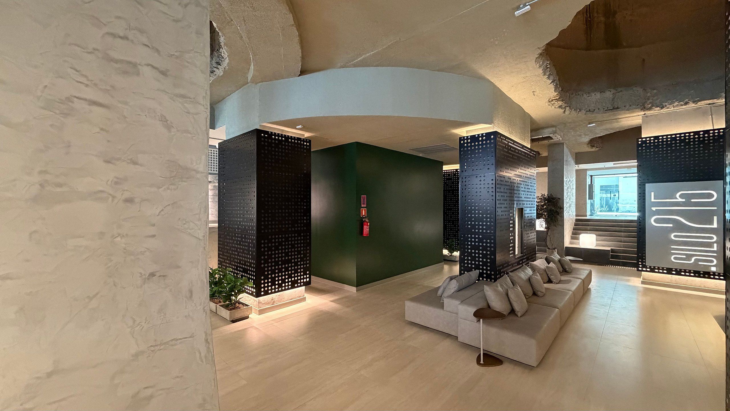 Un interior moderno con techo curvo, un sofá modular y un gran pilar negro perforado.