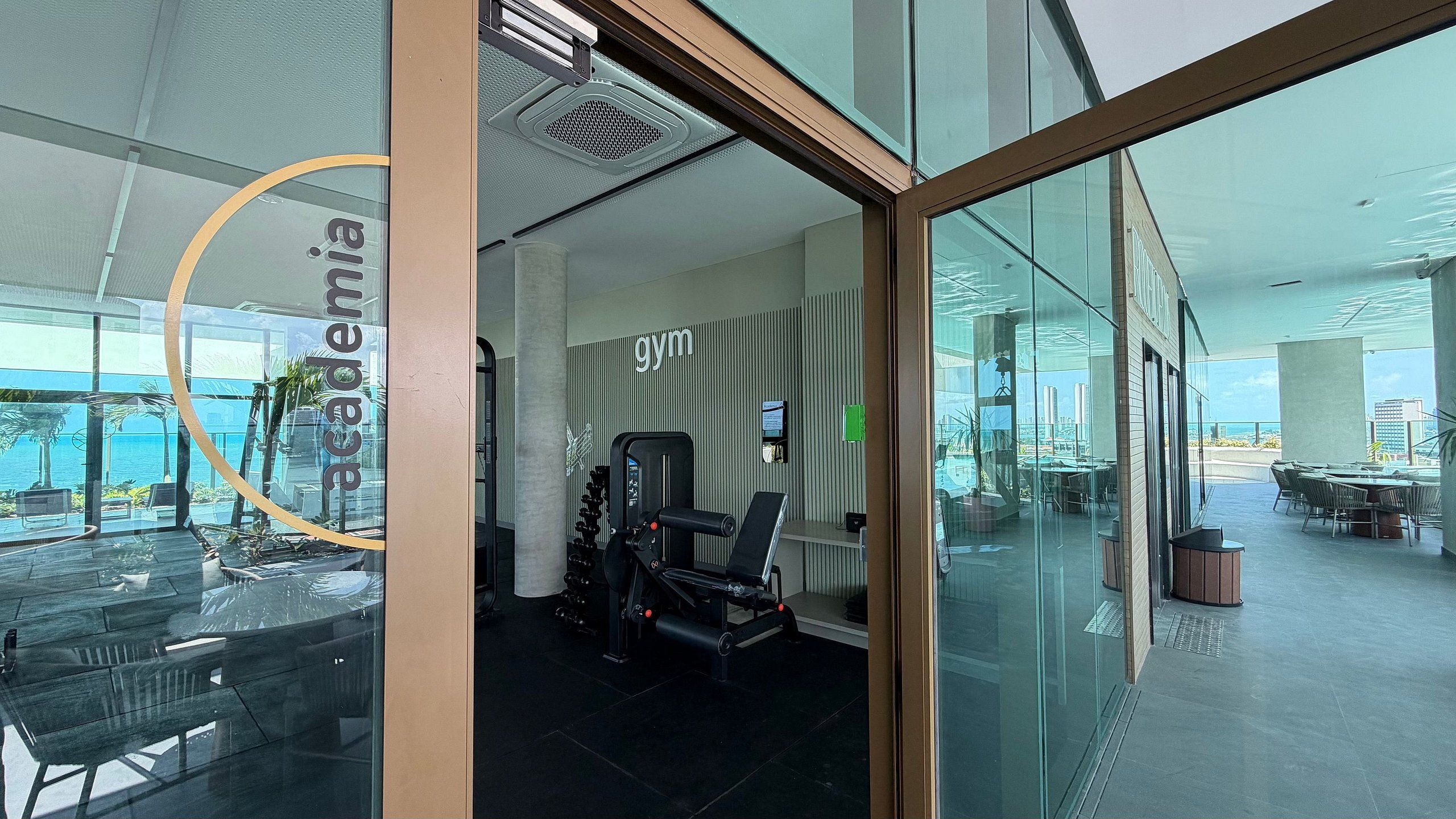 Un gimnasio con equipo de ejercicio, un ventanal y vista al océano.