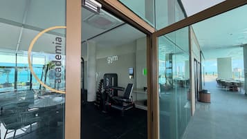 Un gimnasio con equipo de ejercicio, un ventanal y vista al océano.