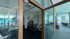 A gym with exercise equipment, a large window, and a view of the ocean.