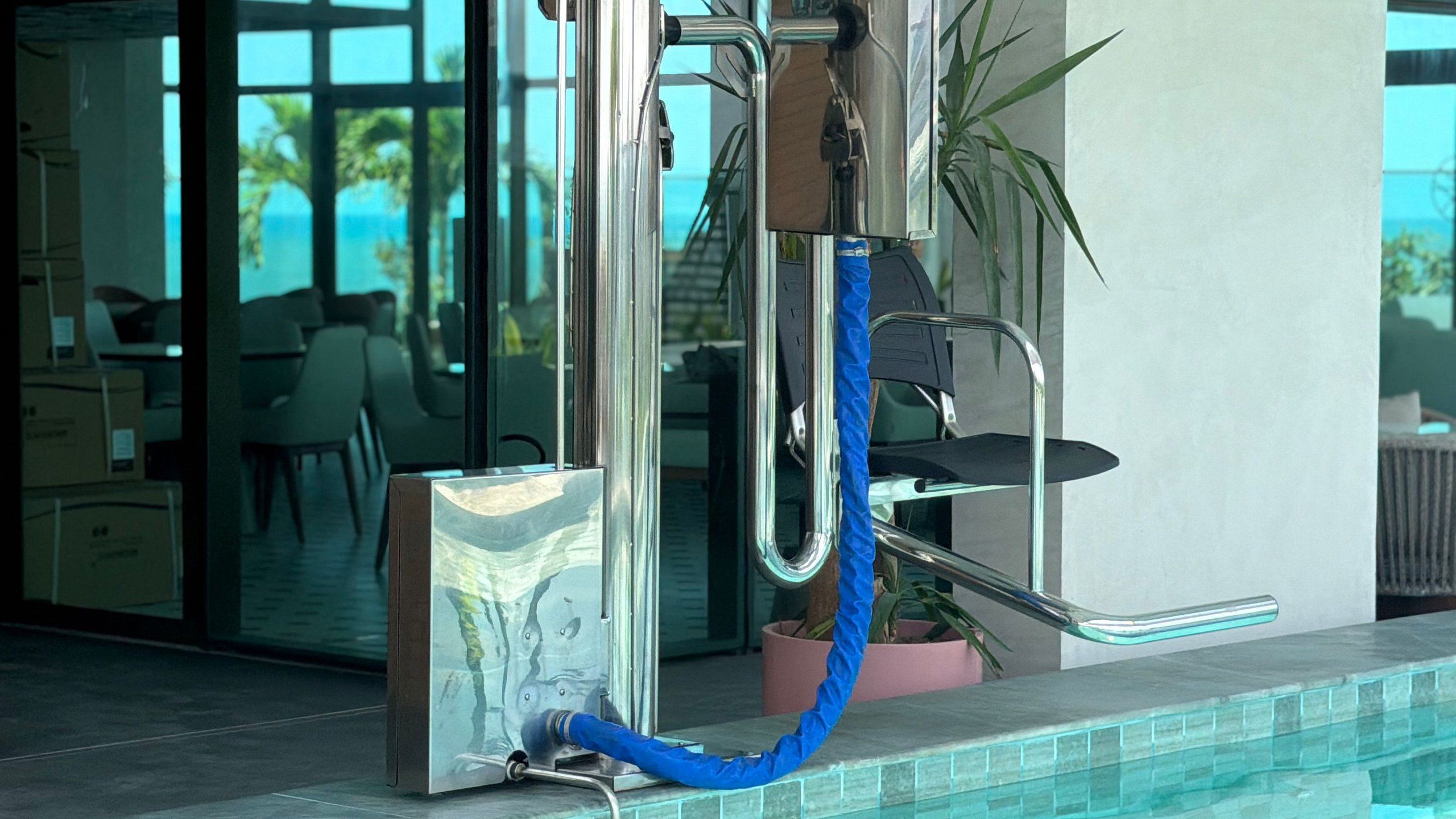 Un baño moderno con cabina de ducha de vidrio, un manguera azul y una planta en maceta.
