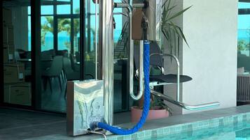 Un baño moderno con cabina de ducha de vidrio, un manguera azul y una planta en maceta.