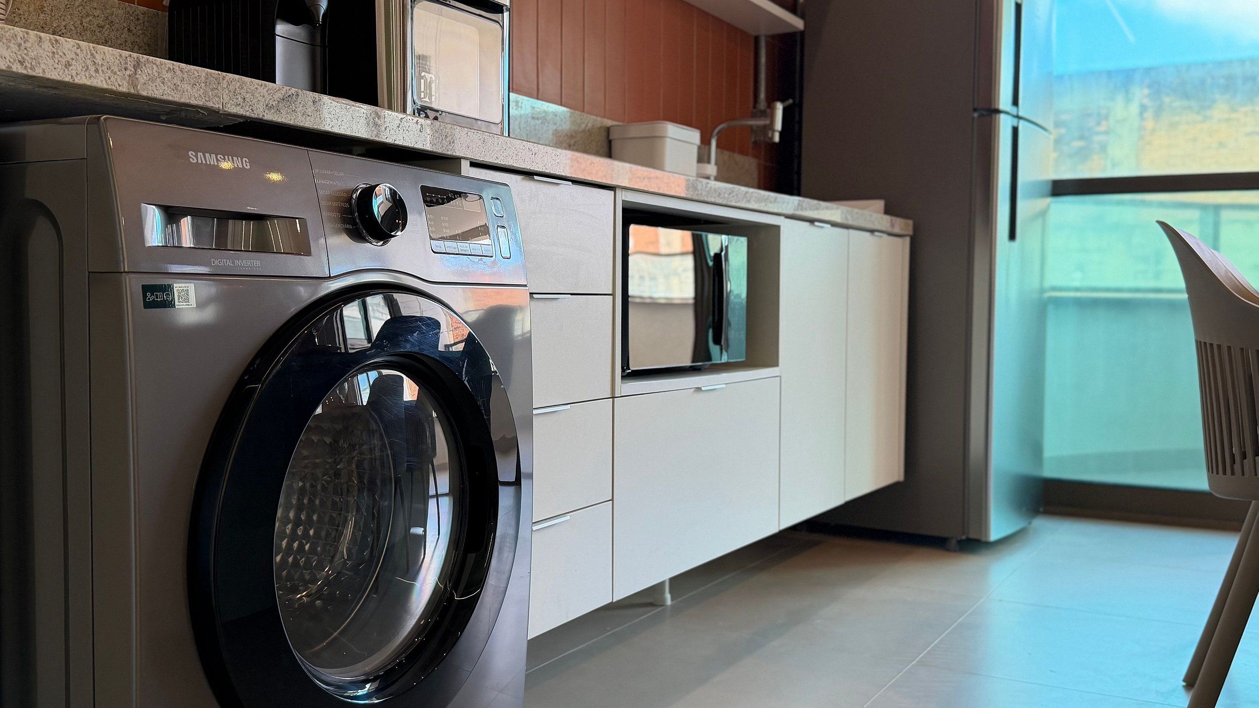 A compact kitchen with a built-in washing machine, a window, and a view of the outdoors.