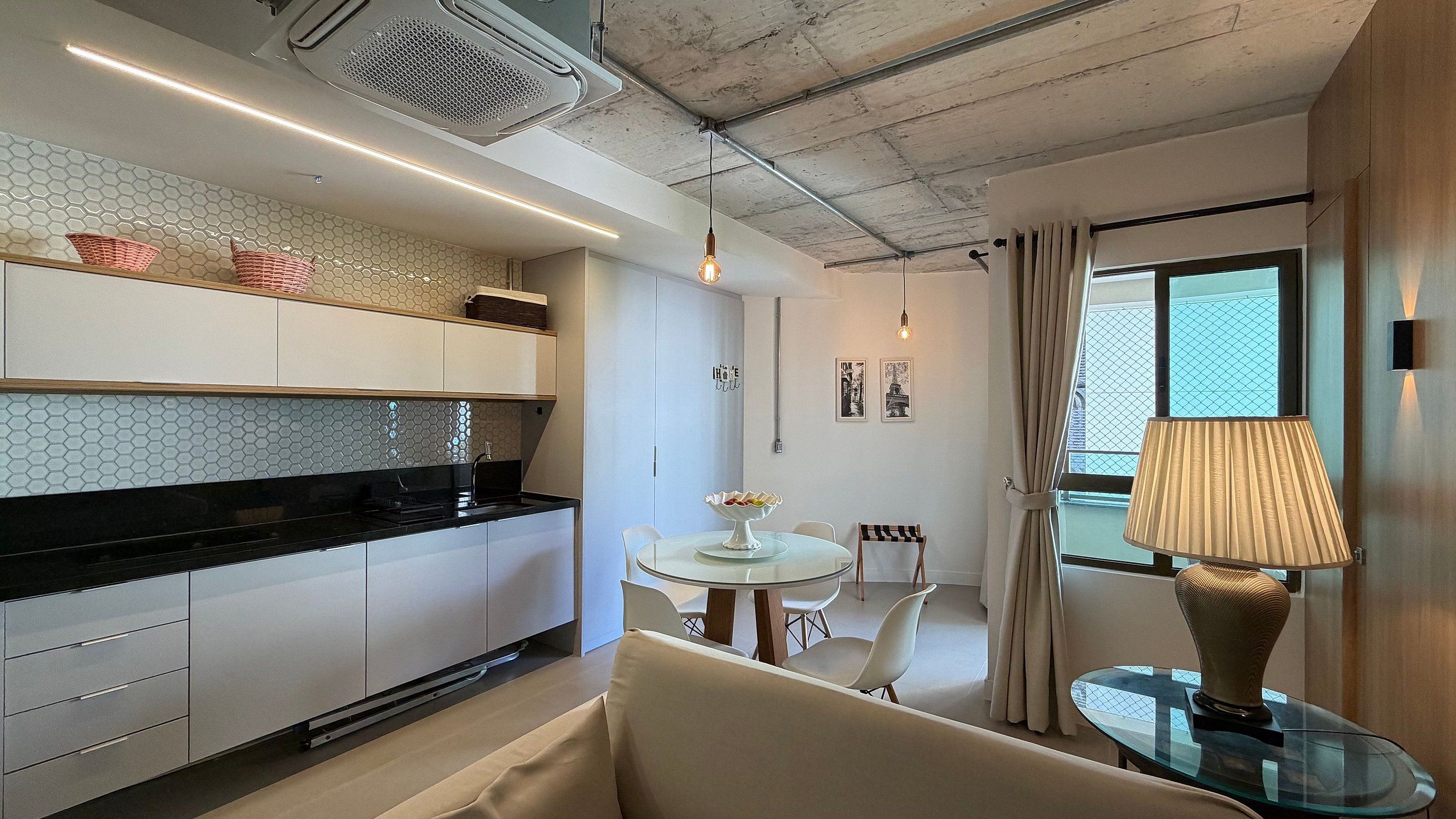 A modern kitchen with white cabinets, a black countertop, and a dining area with a glass table and white chairs.