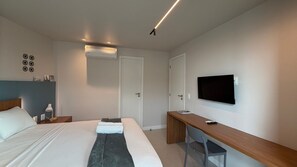 A hotel room with a bed, a desk, a chair, a television, and a door.