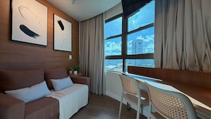A modern living room with a sofa, a dining table, and a view of a cityscape through large windows.