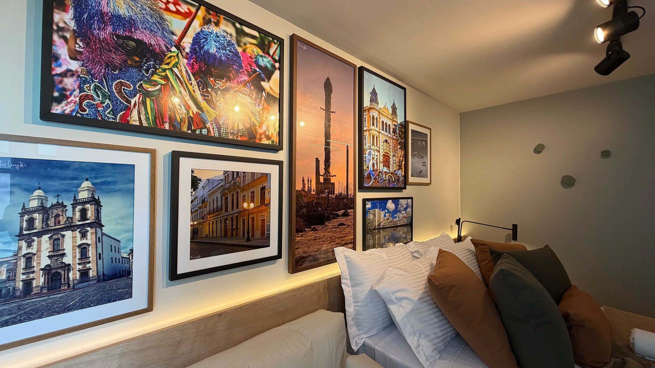 A hotel room with a bed, pillows, and a wall decorated with framed pictures of various buildings and cityscapes.