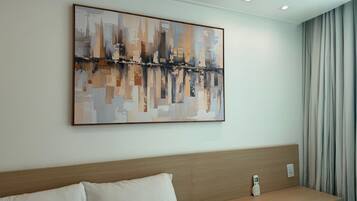 A hotel room with a large abstract painting on the wall, a wooden headboard, a white pillow, and a bedside table with a remote control.