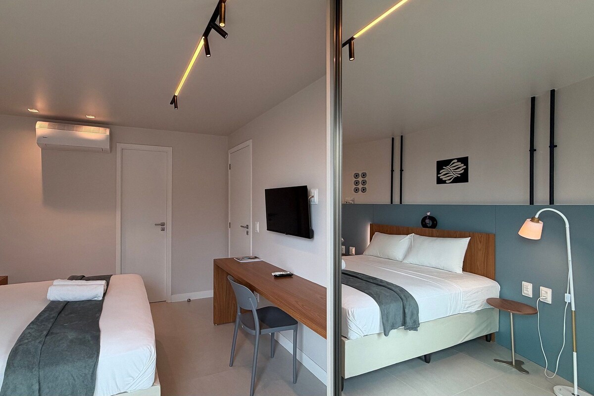 A modern hotel room with two beds, a desk, a TV, and a mirror.