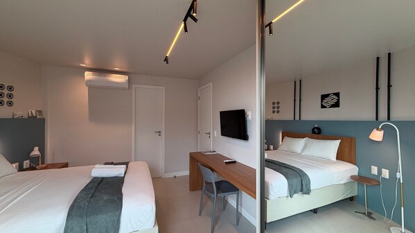 A modern hotel room with two beds, a desk, a TV, and a mirror.