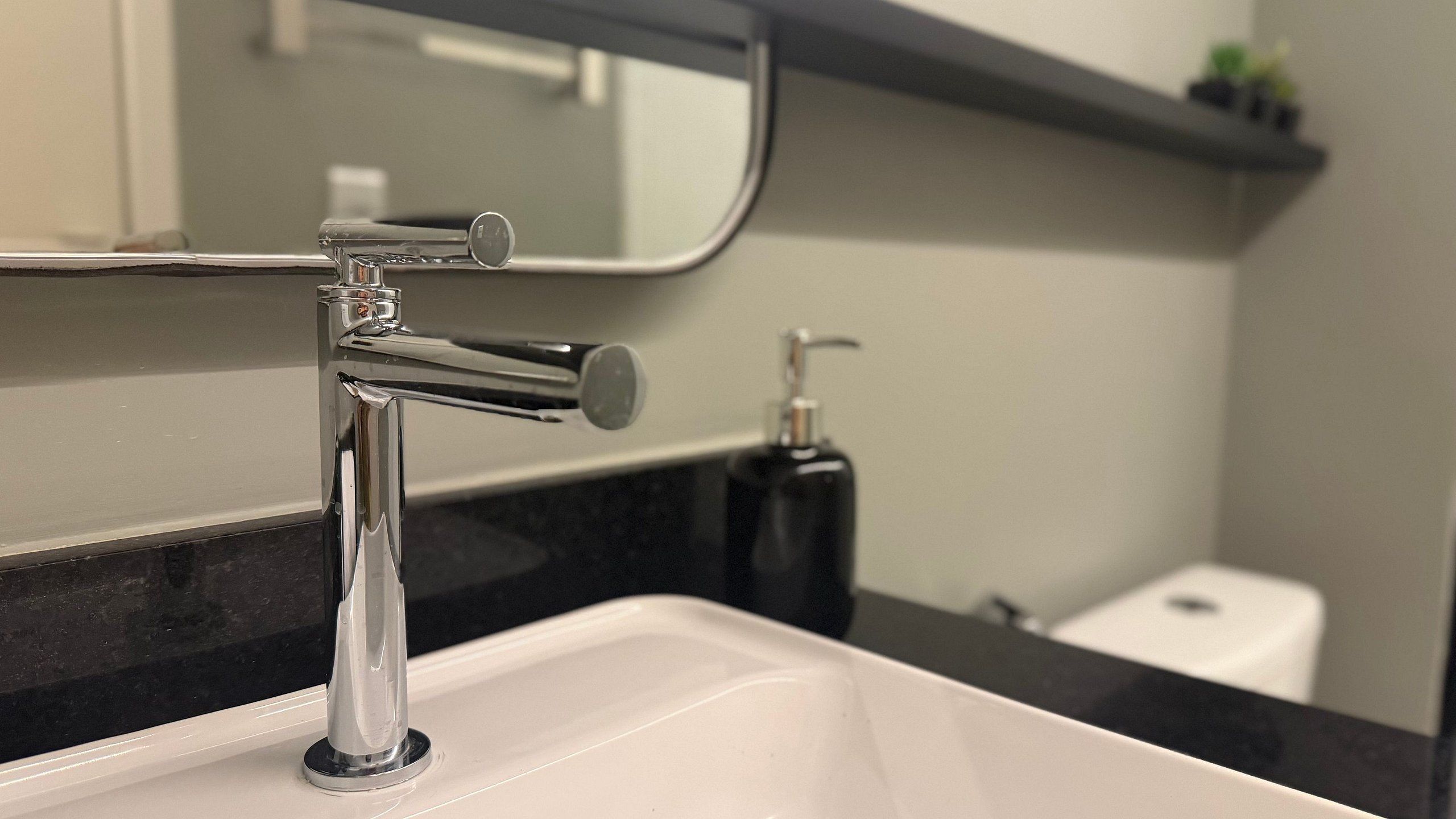 Un lavabo con grifo cromado, un espejo y un dispensador de jabón en la encimera.