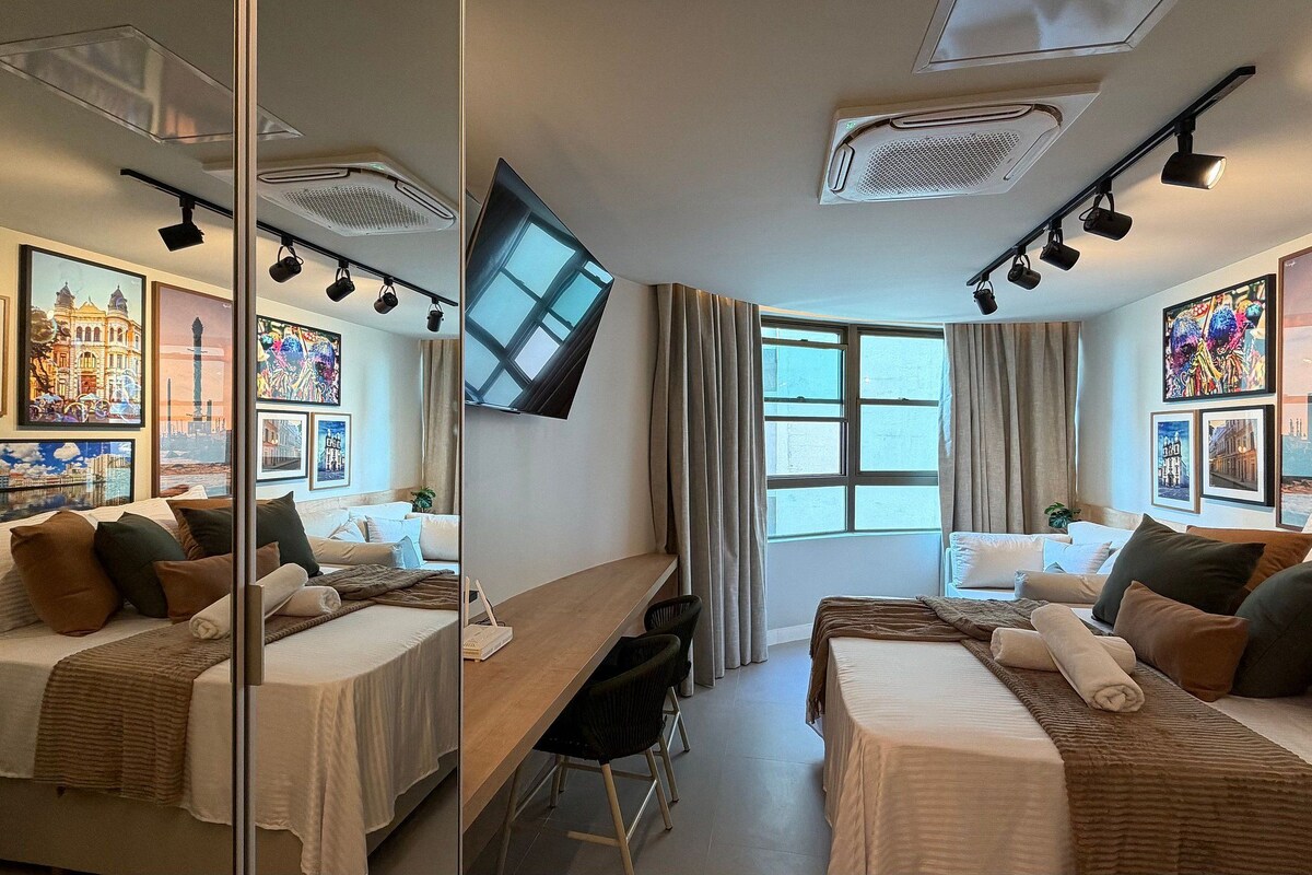 A hotel room with two beds, a desk, a flat-screen TV, and artwork on the walls.