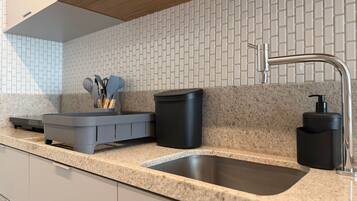 A kitchen with a granite countertop, a stainless steel sink, a black trash bin, a soap dispenser, and a utensil holder.