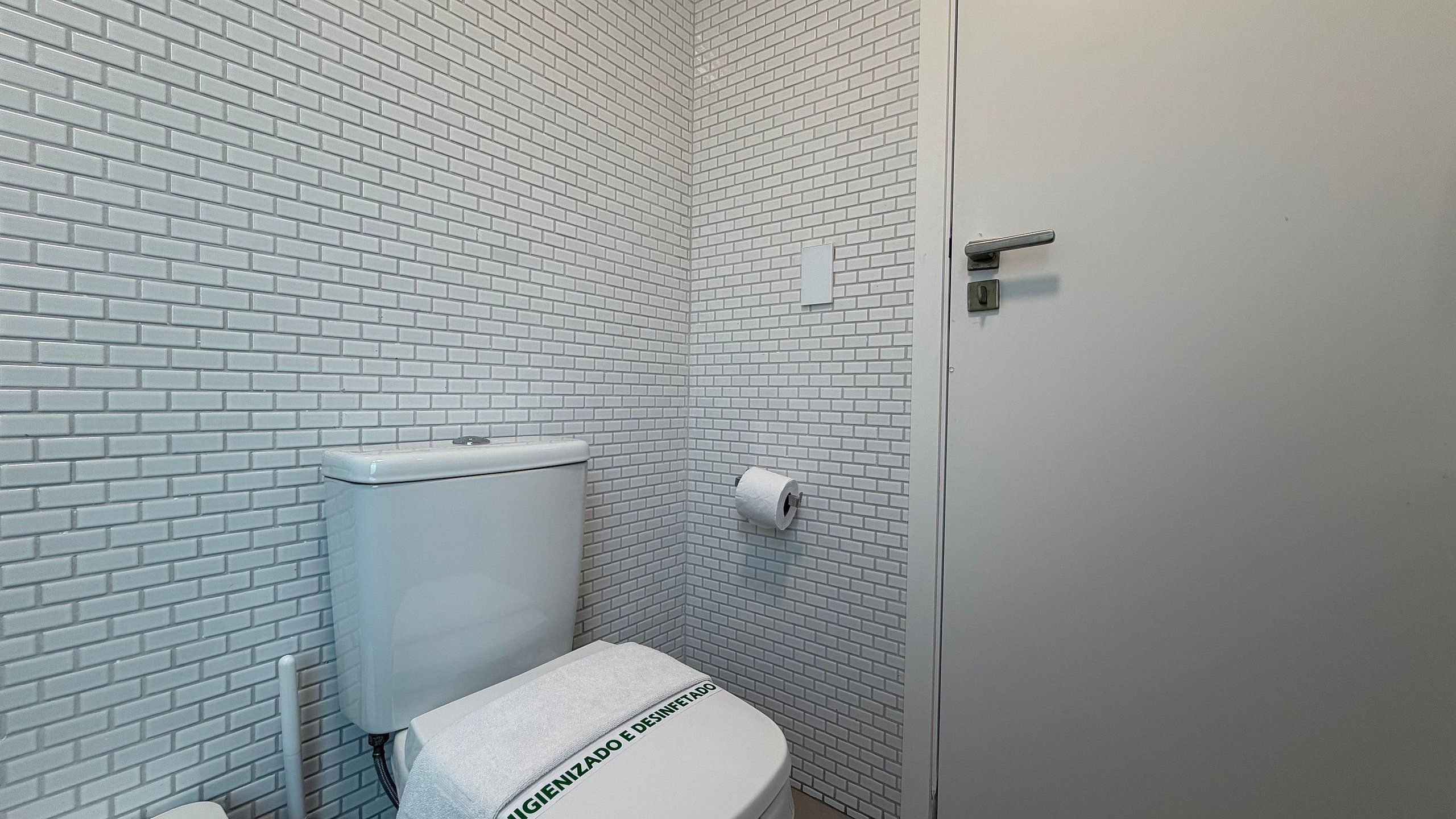 Un baño pequeño con azulejos blancos, un inodoro y un rollo de papel higiénico.