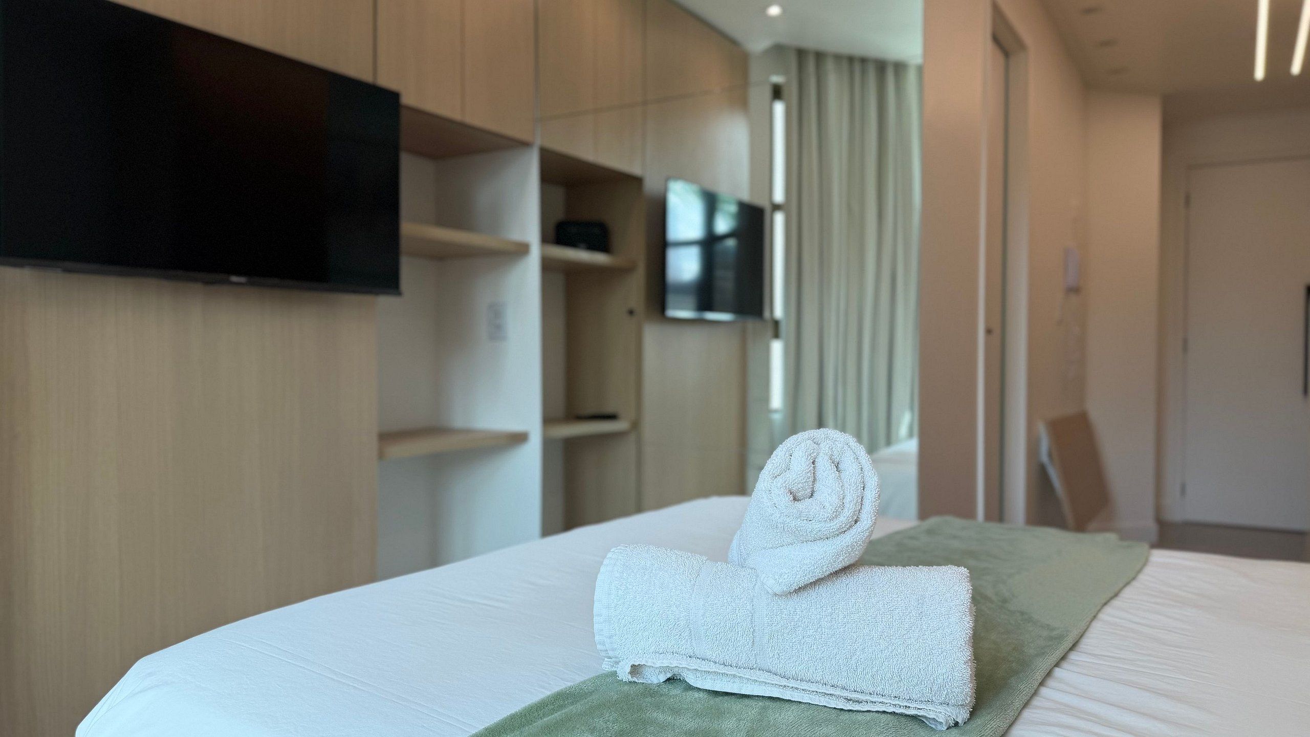 Una habitación de hotel con una cama bien hecha, un televisor de pantalla plana en la pared y un armario de madera.