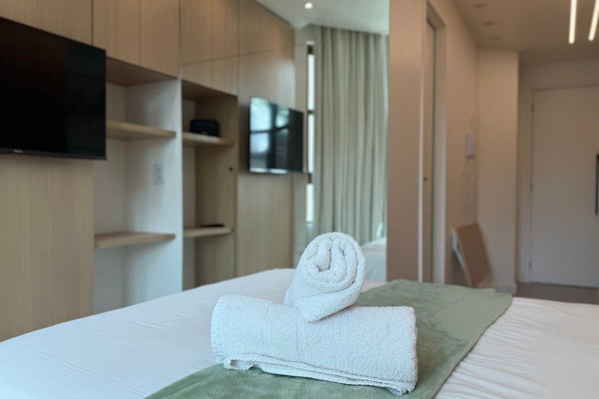 A hotel room with a neatly made bed, a flat-screen TV mounted on the wall, and a wooden wardrobe.