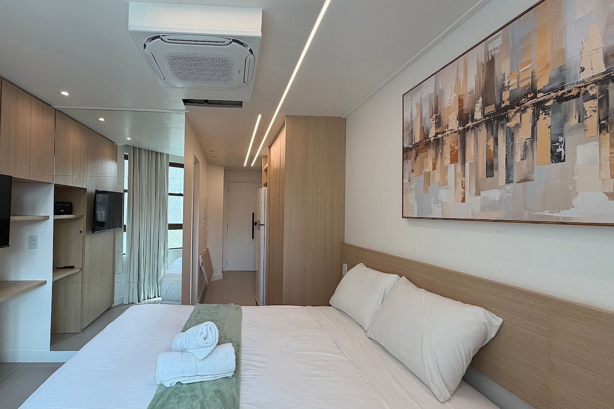 A modern hotel room with a large bed, a flat-screen TV mounted on the wall, and a painting above the bed.