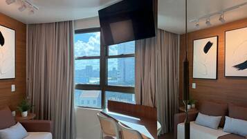A modern hotel room with a large window, a flat-screen TV, and artwork on the walls.