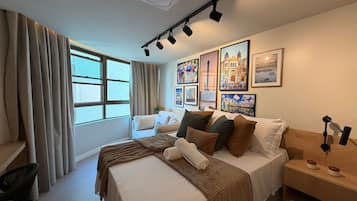 A hotel room with a bed, a bedside table, a lamp, a window with curtains, and wall art.