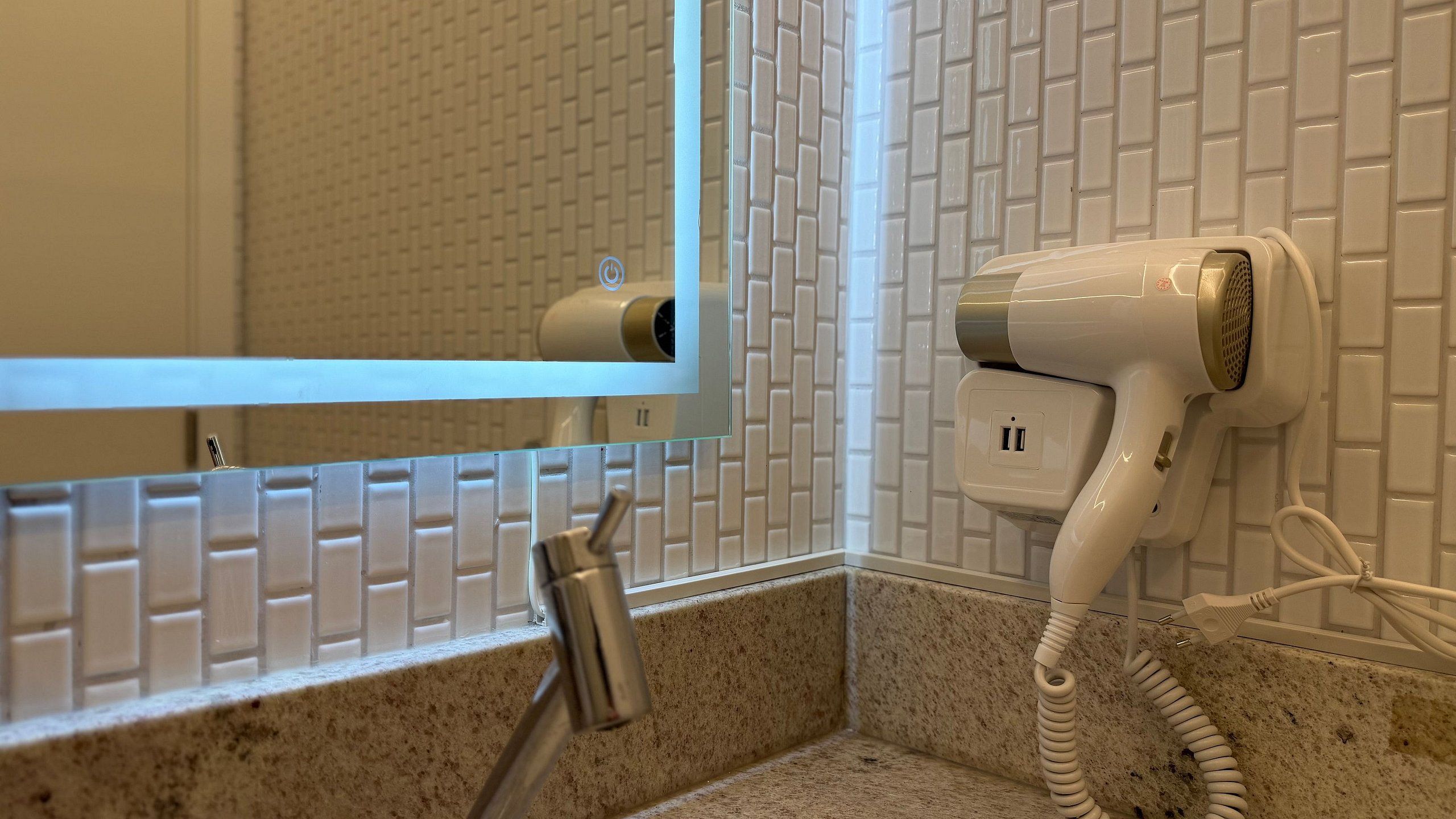 A bathroom with a hairdryer mounted on the wall, a mirror, and a sink with a faucet.