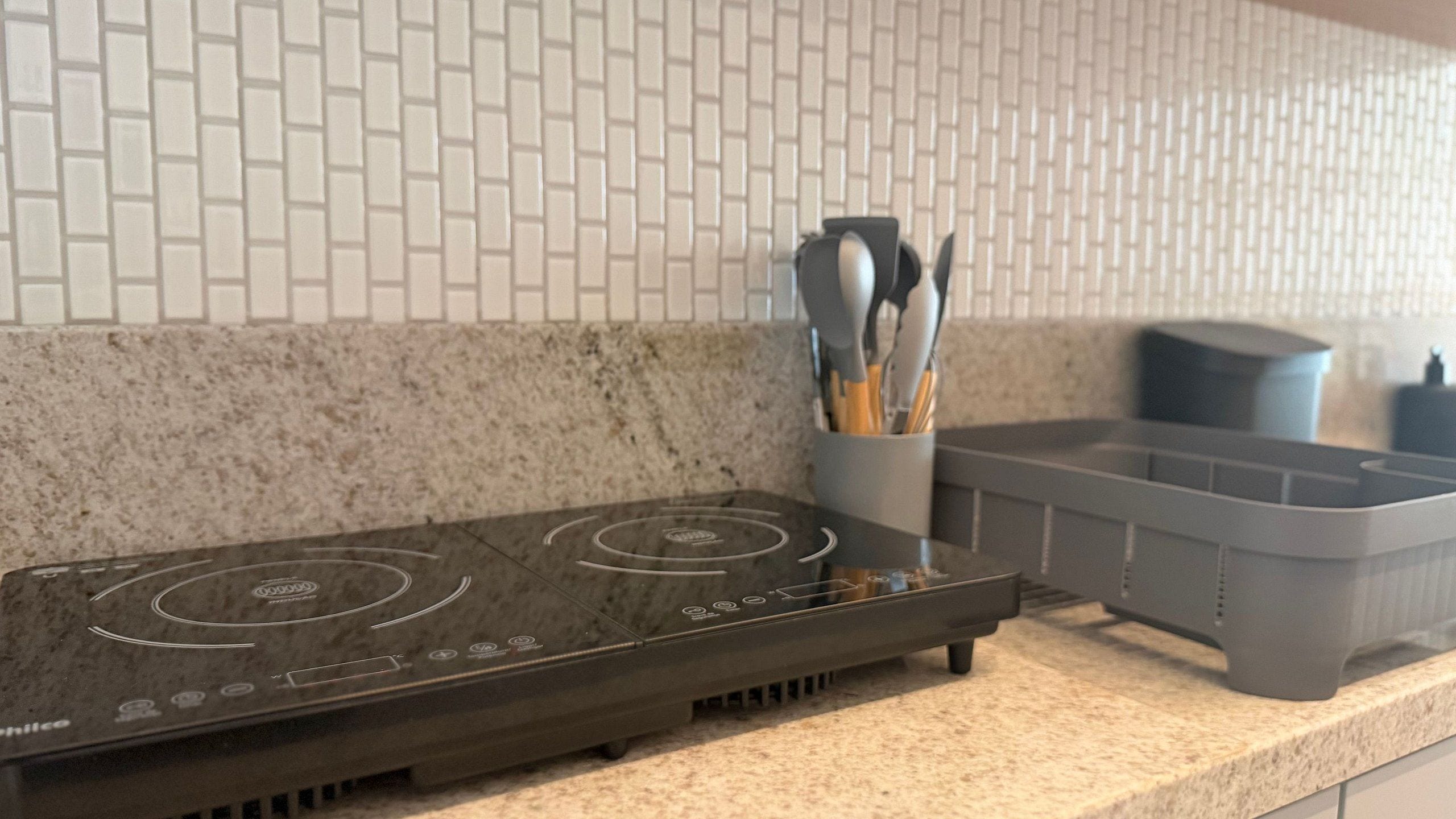 Una cocina con tope de inducción negro, encimera de granito y salpicadero de azulejos blancos tipo metro.