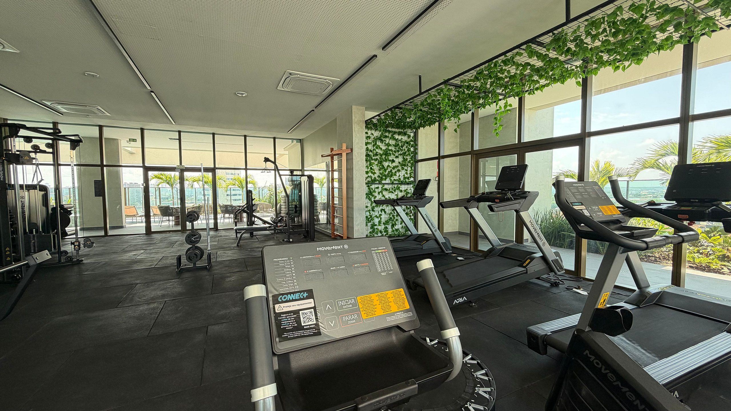 Un gimnasio con cintas de correr, máquinas de pesas y una pared cubierta de vegetación.