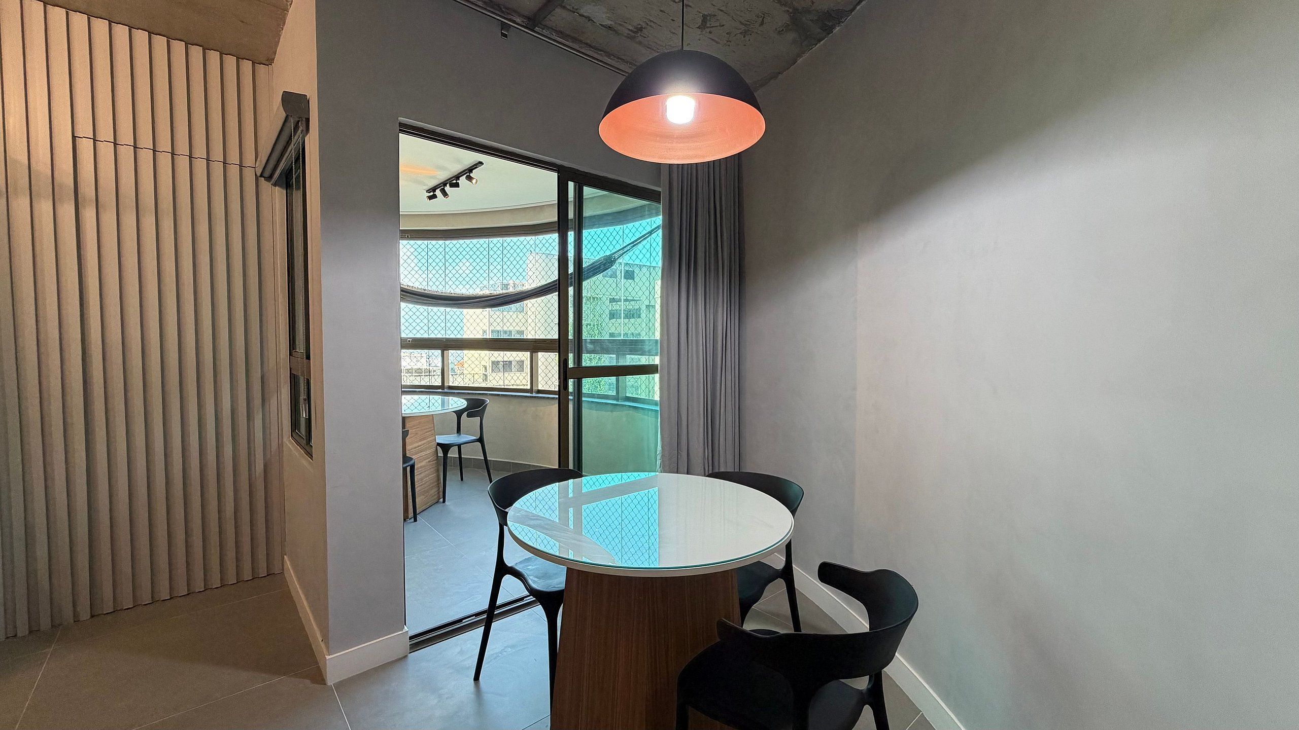 A modern interior with a round table, black chairs, a hanging pendant light, and a view through large windows.